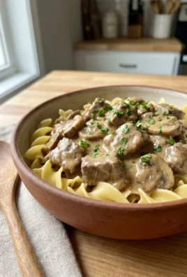 A close-up shot of beef stroganoff in a white bowl with a fork.