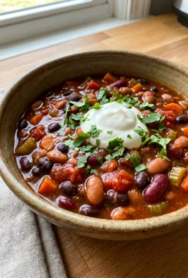 A spoon stirring thick red vegetarian chili inside of a black slow cooker.
