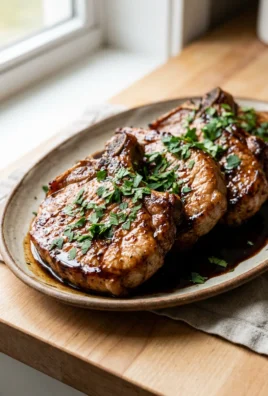 A white plate holding a cooked pork chop topped with a dark glaze and fresh parsley.