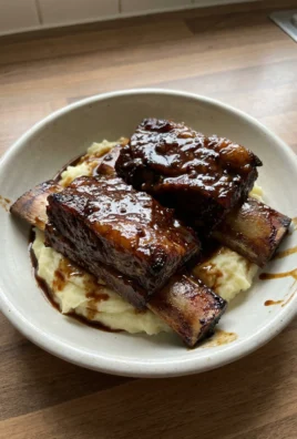 A close-up of a fork cutting into a tender piece of a slow-cooked short rib.