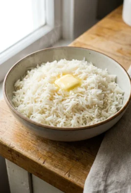 A white ceramic bowl filled with cooked, fluffy white rice on a wooden table.
