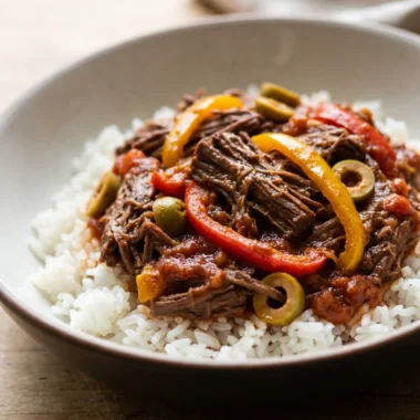 A white bowl filled with shredded ropa vieja, garnished with fresh cilantro and a lime.