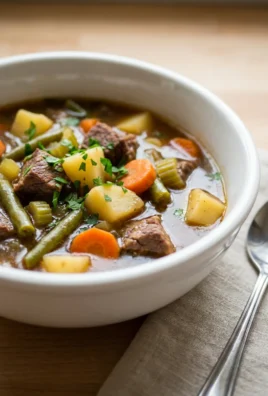 A close-up of a spoonful of hearty veggie beef soup showing meat and vegetables.